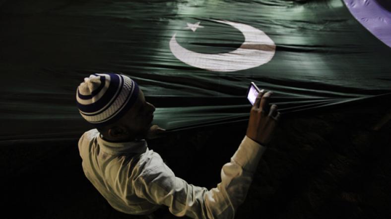 Pakistan bayrağı önünde cep telefonuyla görüntü alan bir Pakistanlı.