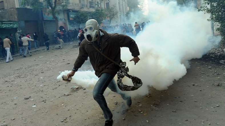 Gaz maskeli bir gösterici polisin attığı gaz bombasını taşıyor.