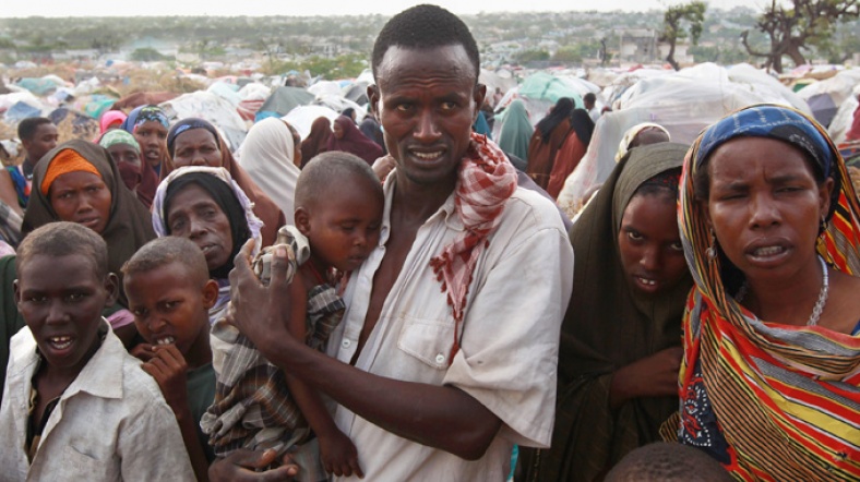 Kucağında çocuğuyla yemek sırası bekleyen Somalili erkek.
