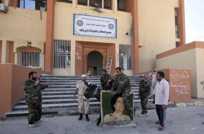 Eşeğe bağlanmış Kaddafi posteri ve etrafında UGK askerleri.