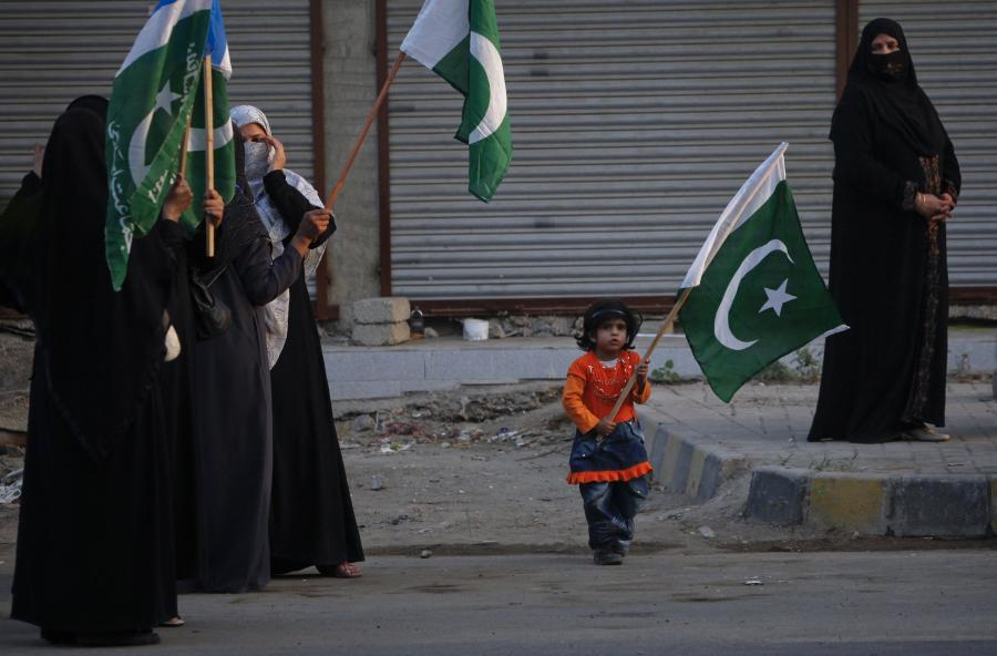 Kadınlar ve bir çocuk Pakistan bayrağı sallıyor.